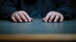Hvem er han? Manden bag hænderne på bordfladen hos politiet. Han forbliver et mysterium i 'Børnelokkeren'. Foto: Still/DR