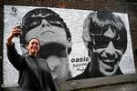 Emily McShane, der er fan af Oasis, tager en selfie foran et artwork af Oasis' Liam and Noel Gallagher i Manchester i tirsdags.  Foto: Paul Ellis/Ritzau Scanpix