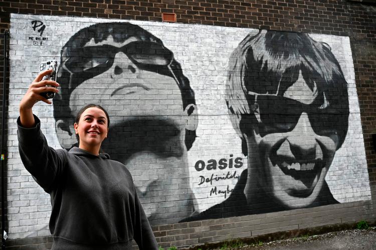 Emily McShane, der er fan af Oasis, tager en selfie foran et artwork af Oasis' Liam and Noel Gallagher i Manchester i tirsdags.  Foto: Paul Ellis/Ritzau Scanpix