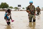 En pige med et lille barn går forbi en FN-soldat i delstaten Boma i Sydsudan, hvor voldsom regn har sendt hundredtusinder på flugt.  Foto: Reuters/Ritzau Scanpix