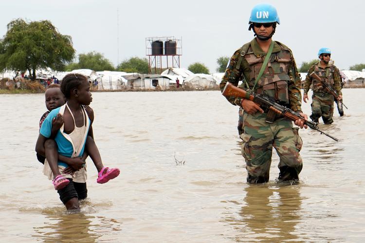 En pige med et lille barn går forbi en FN-soldat i delstaten Boma i Sydsudan, hvor voldsom regn har sendt hundredtusinder på flugt.  Foto: Reuters/Ritzau Scanpix