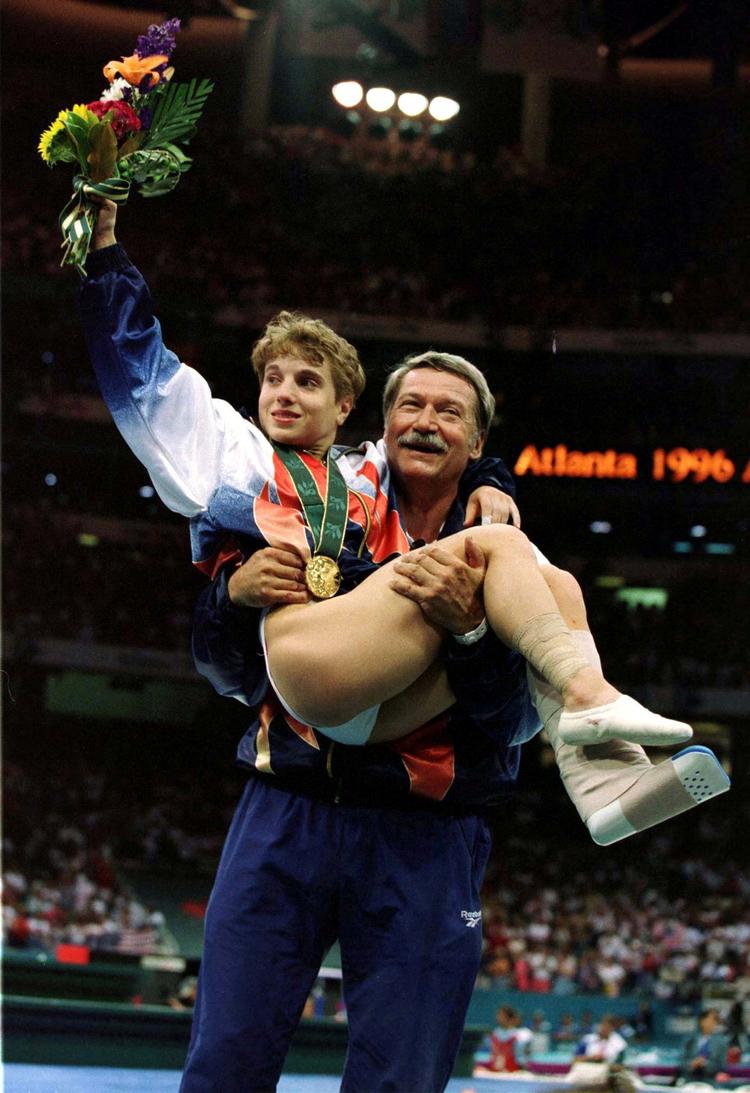 Béla Károlyi bærer Kerri Strug ned fra sejrspodiet, efter at den amerikanske gymnast har fået overrakt en guldmedalje ved OL i 1996. Strugs forhold til sin træner var ligesom flere andres kompliceret.  Arkivfoto:  Mike Blake