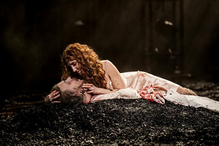 Salome i skikkelse af sopranen Laura Wilde kysser længe og begærligt med Johannes Døberens afhuggede hoved. Scenen er dækket af sort aske. Foto: Jonas Persson