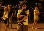 En person holder sin hund tæt ind til sig og står sammen med andre foran deres lejlighedsbygning, som blev ramt af et russisk droneangreb i Kyiv 10. juli 2025. Foto: Stringer/Ritzau Scanpix