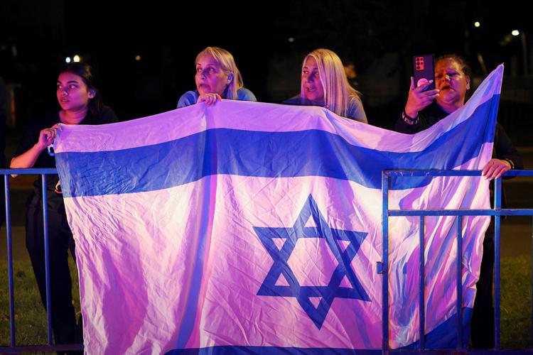 Kvinder synger nationalsangen, mens en konvoj passerer forbi med lig fra Gaza til Israel. Ligene fragtes til en retsmedicinsk afdeling, hvor de identificeres. Hamas har udleveret otte lig, og syv af dem var på den israelske liste over savnede. Israel har udleveret mindst 45 dræbte palæstinensere til Gaza. Foto: Stoyan Nenov/Ritzau Scanpix