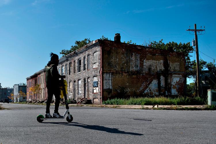 En mand kører på en scooter forbi forladte huse i kvarteret Broadway East i Baltimore. Området har overvejende afroamerikanske indbyggere. Det er fattigt og ødelagt af årtiers forsømmelse, hvilket står i skarp kontrast til de dyre ejerlejligheder, nye butikker og trygge gader et par kilometer væk i overvejende hvide og velhavende områder i byen.. Foto: Brendan Smialowski/Ritzau Scanpix