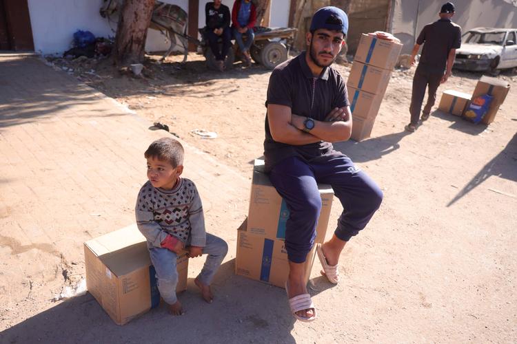 En palæstinensisk mand og et barn sidder på madrationeringskasser fra Verdensfødevareprogrammet (WFP) i landsbyen Al-Zawayda i det centrale Gaza. Hjælpeorganisationer klager over, at humanitære konvojer stadig ikke har tilstrækkelig adgang til Gaza. Foto: Bashar Taleb/Ritzau Scanpix