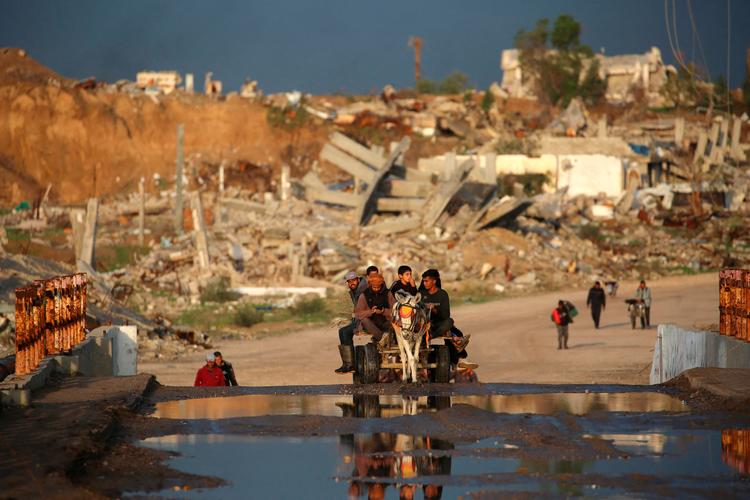 Palæstinensere kører på en æselvogn forbi bygninger og ødelagte hjem i Nuseirat i Gaza-striben. Mindst 16 mennesker døde af kulde under en vinterstorm forleden. Kraftig regn fra stormen Byron oversvømmede telte og midlertidige beskyttelsesrum over hele Gaza.   Foto: Eyad Baba/Ritzau Scanpix