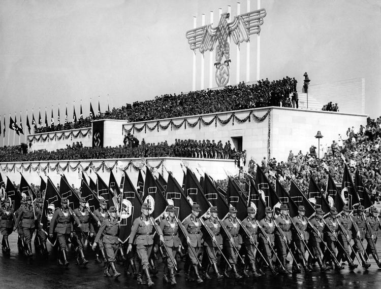 Ved Rigspartidagene i 1935 marcherer flagbærere forbi tribunen på Zeppelinfeld, hvorfra Adolf Hitler selv kunne overvåge paraden sammen med andre topnazister. Foto: archiv für Zeitgeschichte/a/Ritzau Scanpix