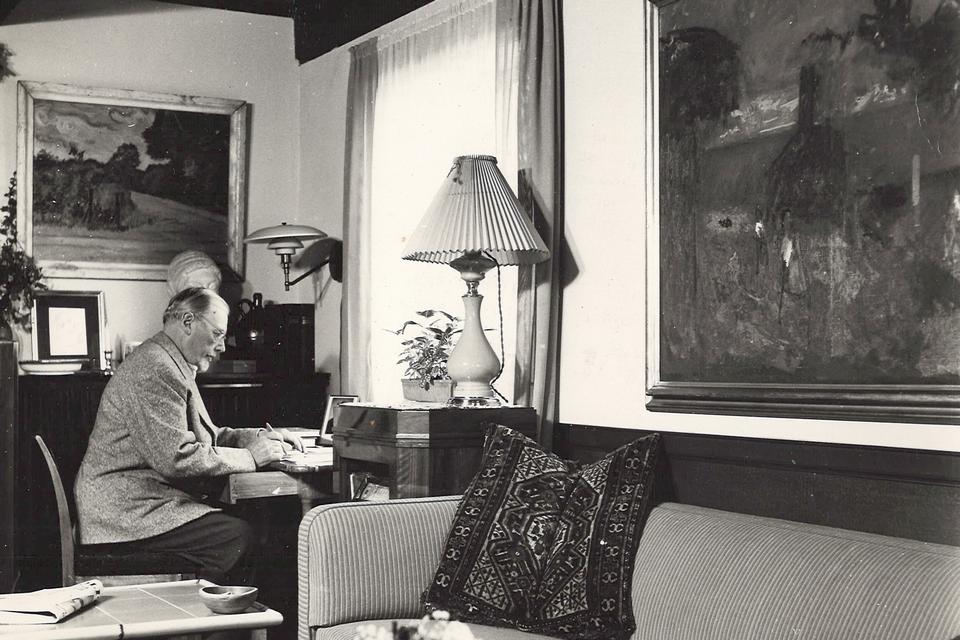 Fotografiet er fra 1950'erne og viser Oluf Høst, der sidder i stuen i hjemmet i Gudhjem og arbejder. Foto: Oluf Høst Museet