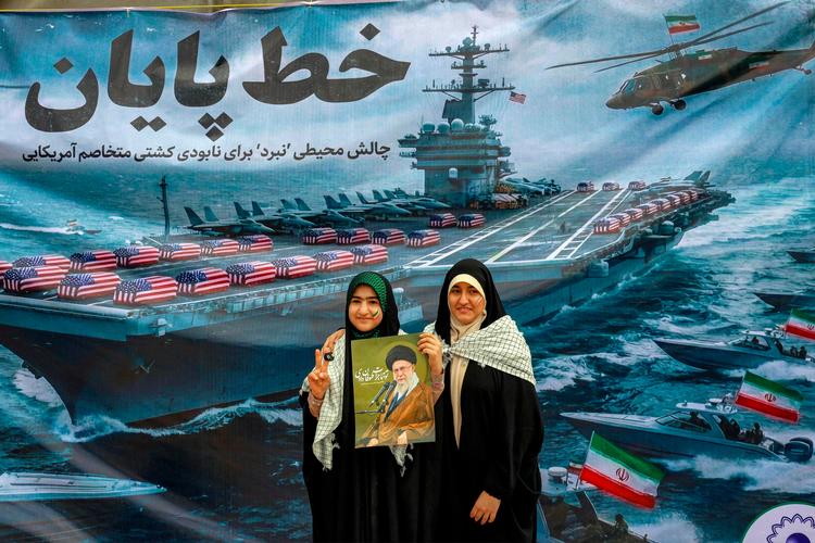 Iranske kvinder poserer med et foto af ayatollah Khamenei, mens de står foran et banner, der forestiller et amerikansk flådehangarskib med kister indhyllet i amerikansk flag på dækket. Foto: -/Ritzau Scanpix