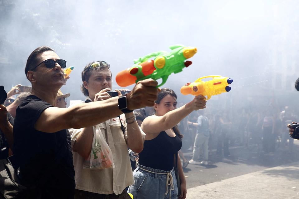 En gruppe demonstranter sprøjter vand fra vandpistoler mod gæster på en café i Barcelona i juni 2025. Foto: Bruna Casas/Ritzau Scanpix