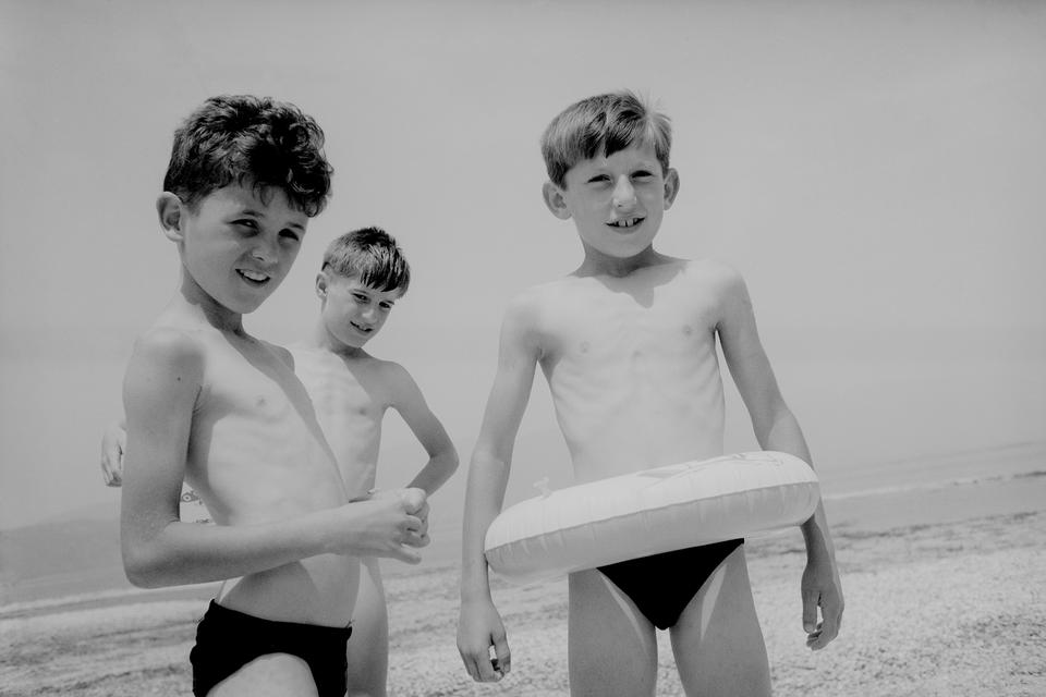 (Ohrid-søen, Makedonien, 1994).  »Midt i krigen mødte jeg pludselig min egen barndom. De tre drenge ved vandet var som et deja-vu fra Furesøbadet i Virum, hvor jeg lærte at svømme. Jeg havde de samme tynde arme, de samme badebukser og den samme badering. Det var ikke et billede til dagens avis – men et billede om håb, møder og de historier, man finder mellem aftalerne«.  Foto: Carsten Ingemann/INGEMANN PHOTOGRAPHY