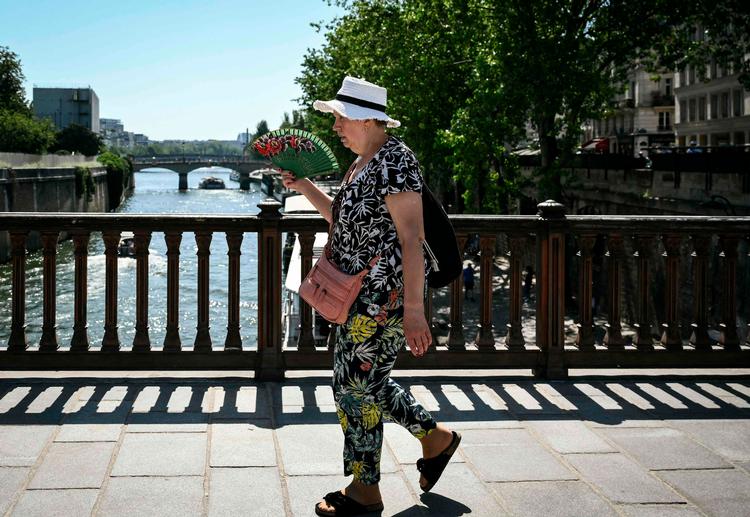 En kvinde passerer Seine-floden, mens hun forsøger at køle sig ned med en vifte. 26 millioner franskmænd bor i et område, som i søndags fik rød hedebølgealarm fra den nationale vejrtjeneste, Météo. Foto: Arnaud Finistre/Ritzau Scanpix