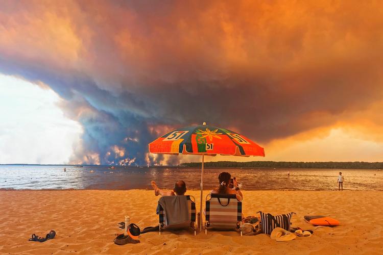 Fra stranden Moutchic i det sydvestlige Frankrig kan solbadende turister se over på røgskyerne fra naturbrande  24. juli. Rekordstore områder er brændt af i Frankrig denne sommer. Foto: Maximilien Lamy/Ritzau Scanpix