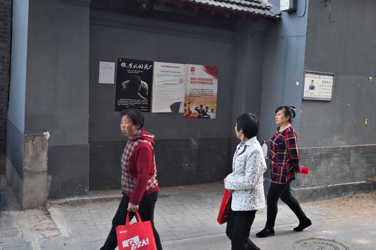 Lokale i centrum af Beijing går forbi en mur, hvor plakaten i midten opfordrer dem til at være på udkig efter spioner. 