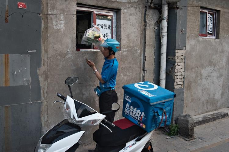 Et mand køber varer i en af de købmandsbutikker i centrum af Beijing, der har fået facaden muret til, så der nu kun er et lille vindue. 