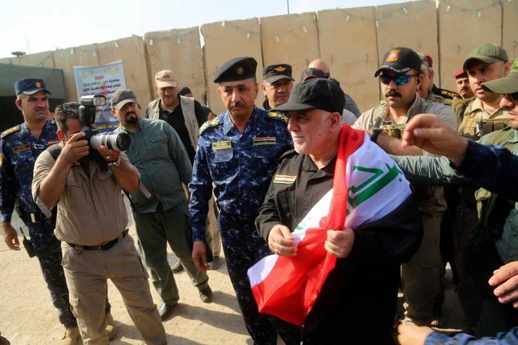 Iraks premierminister, Haida al-Abadi, holdt det irakiske flag ved sin ankomst til Mosul søndag, hvor han erklærede byen tilbageerobret fra IS. Med hjælp fra den USA-ledede koalition indledte den irakiske hær tilbageerobringen af byen i oktober 2016. 