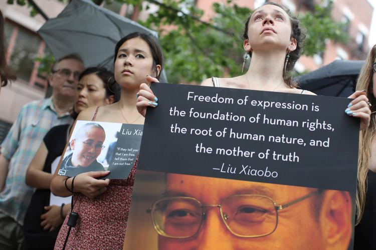 Demonstranter i New York holder torsdag efter meddelelsen om Liu Xiaobos død plakater med billeder af ham og hans kone. 