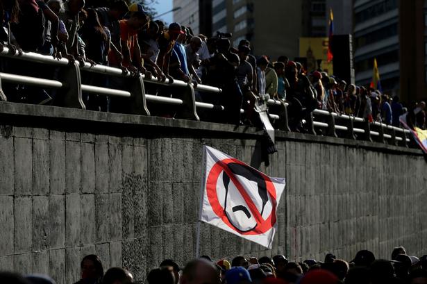 I går, søndag, kulminerede urolighederne, da venezuelanerne skulle stemme om en grundlovgivende forsamling. Den nye forsamling på 545 delegerede kan erstatte det nuværende parlament, hvor oppositionen har haft flertal siden 2015, og forventes ved en forfatningsændring at give præsident Nicolas Maduros socialistparti ubegrænset magt. 
Her holder en demonstrant en fane med en overstreget karikatur af Maduro ved en mindehøjtidelighed for dem, som er blevet dræbt under de daglige protester i dagene op til afstemningen. 