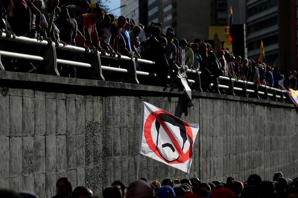 I går, søndag, kulminerede urolighederne, da venezuelanerne skulle stemme om en grundlovgivende forsamling. Den nye forsamling på 545 delegerede kan erstatte det nuværende parlament, hvor oppositionen har haft flertal siden 2015, og forventes ved en forfatningsændring at give præsident Nicolas Maduros socialistparti ubegrænset magt. 
Her holder en demonstrant en fane med en overstreget karikatur af Maduro ved en mindehøjtidelighed for dem, som er blevet dræbt under de daglige protester i dagene op til afstemningen. 