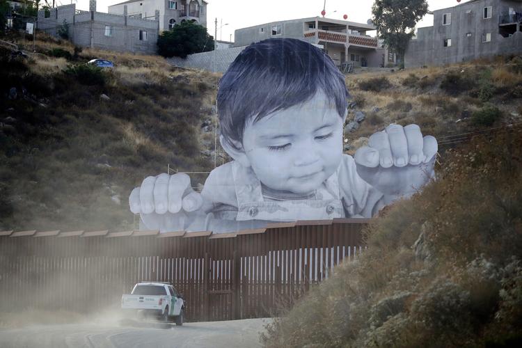 Kunstneren JR's billede af en lille dreng, der måske-måske ikke er på vej til USA over plankeværket fra Mexico, blev opført i onsdags.
AP Photo/Gregory Bull
   