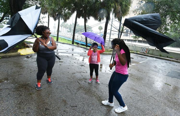 Janesse Brown (tv.) og hendes 12-årige datter Briana Johnson kæmper med blæsten, mens lillesøster Kyra på otte ser til. Billedet er taget i Jacksonville i Florida søndag.  