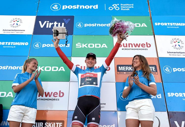 Mads Pedersen jubler på podiet iført den blå førertrøje.
   