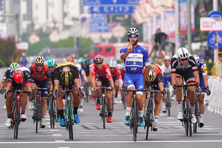 Fernando Gaviria passerer målstregen som vinder af sidste etape i Tour of Guangxi og har overskud til at signalere, at det var hans fjerde sejr i løbet. Magnus Cort, der blev nr. 5, er næsten skjult helt ude til venstre af rytteren med rød hjelm italieneren Andrea Guardini, der besatte fjerdepladsen. Foto: Tim De Waele.
 