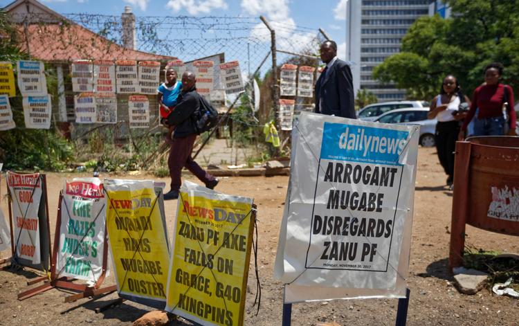 Fodgængere passerer nyhedsskilte i Zimbabwes hovedstad, Harare. Landets mangeårige præsident Robert Mugabe står efter alt at dømme over for en rigsretssag, da han ikke frivilligt vil træde tilbage.   