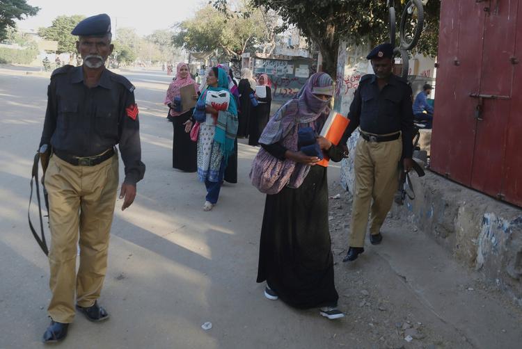 Bevæbnede betjente beskytter sundhedsarbejdere under en vaccinationskampagne i Pakistan. 