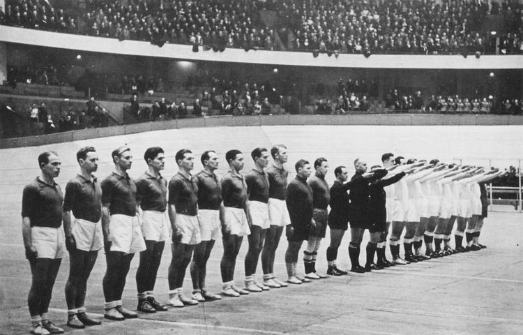 Et - som det vist hedder - ikonisk håndboldbillede fra det første VM i 1938. Danmark møder de senere verdensmestre fra Det Tredje Rige i Deutschlandhalle i Berlin. Danskerne står til venstre, de heilende tyskere til højre. Der var 12.000 tilskuere omkring 6-dagesbanen. Tyskerne vandt 12-3.
   