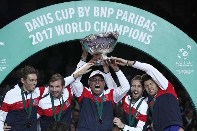 Det franske tennislandshold med holdkaptajn Yannick Noah i midten, iført trofæ, fester efter finalesejren sidste år over Belgien.
    Christophe Ena/AP