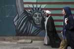 En præst og en kvinde går forbi et anti-amerikansk vægmaleri på muren ind til den tidligere amerikanske ambassade i Irans hovedstad, Teheran.
     Vahid Salemi/AP