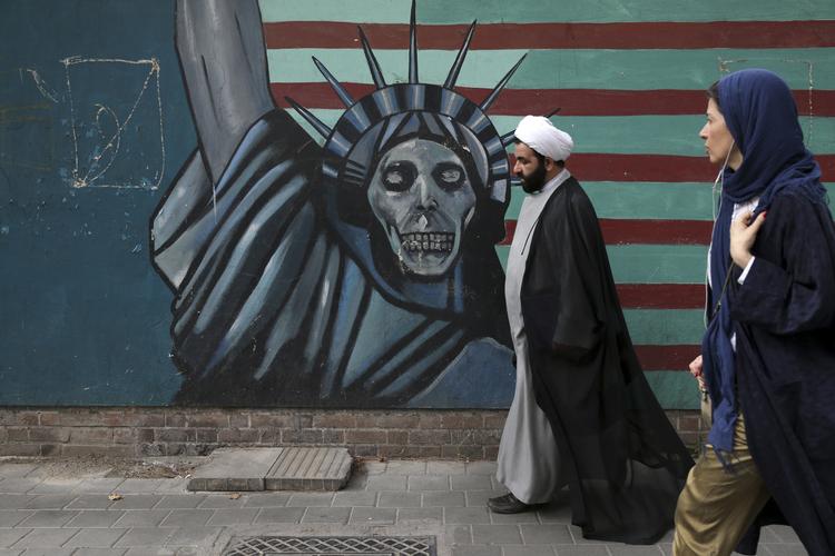 En præst og en kvinde går forbi et anti-amerikansk vægmaleri på muren ind til den tidligere amerikanske ambassade i Irans hovedstad, Teheran.
     Vahid Salemi/AP