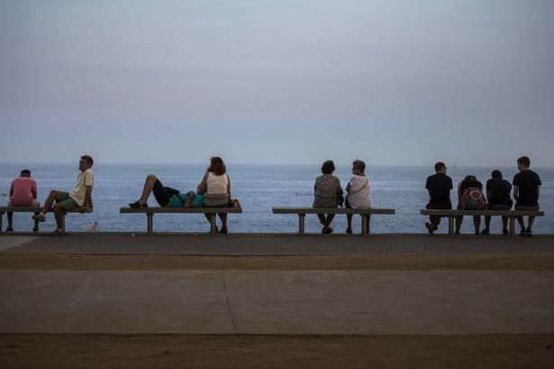 Varmen har drevet folk til kysterne som her, hvor bænkene er optaget langs Barcelonas strand. Emilio Morenatti/AP