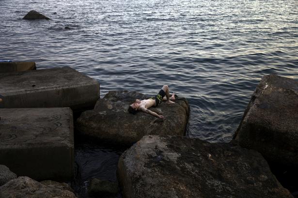 Andre forsøger at finde hvile i vandkanten ved Barcelonas kyst. Emilio Morenatti/AP