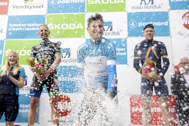 Wout van Aert har indgående erfaring fra sine mange cykelcrosstriumfer i at lade champagnen sprudle, og det fik de omkringstående ved podiet på Frederiksberg Allé at føle. Rasmus Quaade (tv) og Lasse Norman slap dog for en dukkert.
   Thomas Sjørup/Ritzau Scanpix