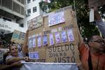 Sygeplejersker fotograferet ved en demonstration i torsdags i Venezuelas hovedstad, Caracas, hvor de med et skilt viser, hvordan deres løn bliver udhulet i takt med, at inflationen stiger.  Ariana Cubillos/AP