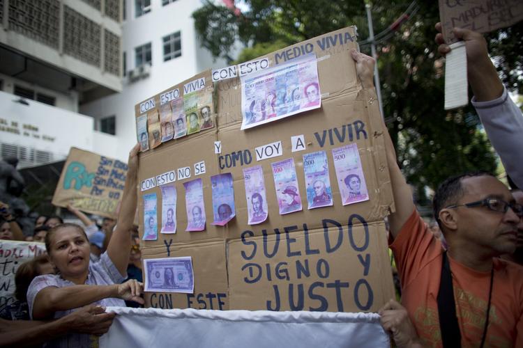 Sygeplejersker fotograferet ved en demonstration i torsdags i Venezuelas hovedstad, Caracas, hvor de med et skilt viser, hvordan deres løn bliver udhulet i takt med, at inflationen stiger.  Ariana Cubillos/AP