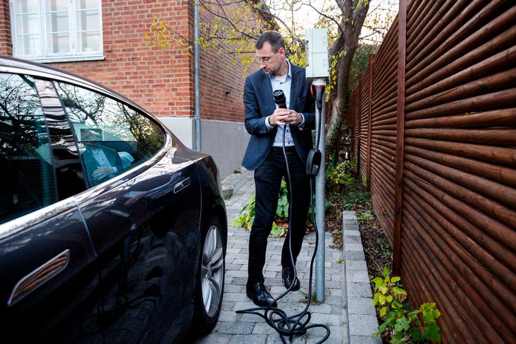 Kasper Jacoby ved elbilens oplader, der ikke er forbundet til husets elsystem. Men i sommer, da solcellerne på husets tag producerede rigtig meget strøm, opladede familien nogle gange bilen fra et stik i huset for at udnytte solen. Andreas Haubjerg/POLFOTO
