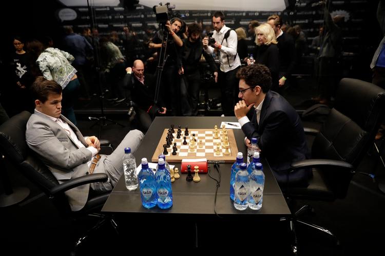 Tilbagelænet i det grå jakkesæt sidder den tredobbelte verdensmester, Magnus Carlsen, og venter på sin modstander. Det gjorde han mange gange under mandagens opgør, hvor Fabiano Caruana brugte god tid på sine træk. Foto: Matt Dunham/AP