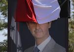 Et billede af den syriske præsident, Bashar Assad, er halvt dækket af det syriske flag. Diktatoren soler sig i, at hans militær – med hjælp fra bl.a. Rusland og Iran er ved at genvinde magten i langt det meste af landet. Foto: Sergei Grits/AP