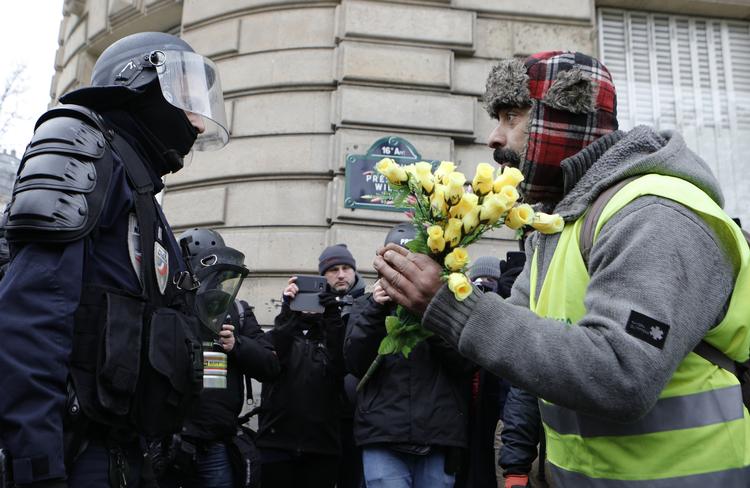 En demonstrant med den karakteristiske gule vest, holder en buket roser foran en politibetjent under en demonstration lørdag 15. december i Paris. Omfanget af weekendens demonstrationen vil give et fingerpeg om, hvorvidt den franske regering er ved at ride stormen af ift. befolkningens utilfredshed.  Foto: Kamil Zihnioglu/AP