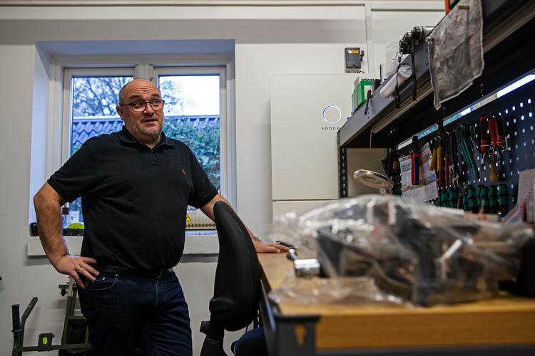 Martin Christensen står ved sit arbejdsbord, hvor man kan se det væghængte batteri i baggrunden. Alt efter årstiderne er familien mere eller mindre selvforsynende med grøn strøm.  Foto: Jan Sommer