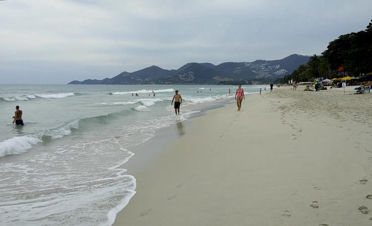 Turister går på stranden Chaweng Beach på øen Koh Samui. Det røde flag markerer, farlige vejrforhold. Øen ruster sig lige nu til den kraftigste storm i mange år, der ventes at ramme øen fredag aften.  Foto: Sithipong Charoenjai/Ritzau Scanpix