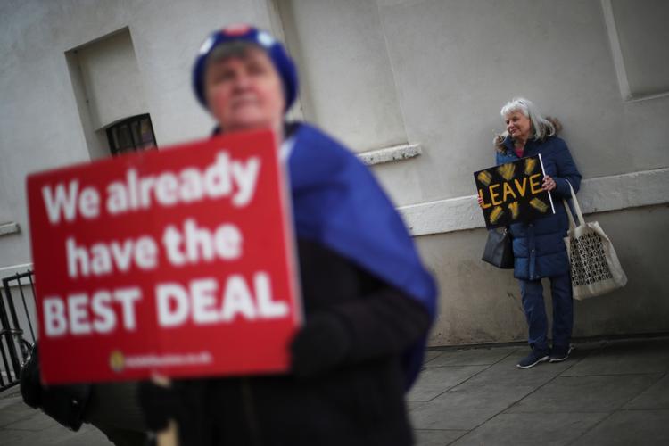 En Brexit-modstander og en tilhænger demonstrerer foran parlamentet med hver deres skilt.  Foto: Hannah Mckay/Ritzau Scanpix