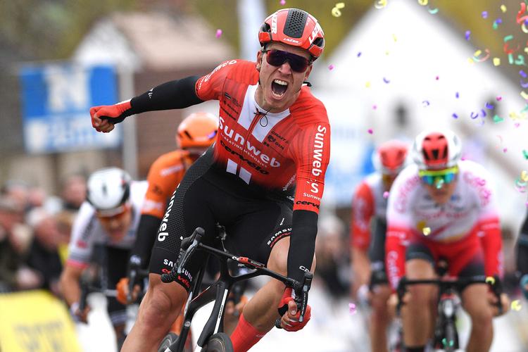 Hollænderen Cees Bol  jubler over at have sikret Team Sunweb sæsonens første sejr, mens landsmanden Mathieu van der Poel lidt længere bagude ligger lidende på brostenene.
 Foto: David Stockman/Ritzau Scanpix