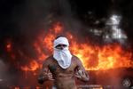 En demonstrant med sten i hænderne foran en brændende busi Caracas, Venezuela. Landet er kastet ud i kaos og kupforsøg.  Foto: Ueslei Marcelino/Ritzau Scanpix