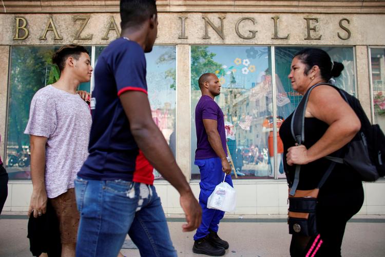Lokale passerer butikker i et shopping område i Havana. Men der er ikke meget på hylderne. Landet er i dyb krise.  Foto: Alexandre Meneghini/Ritzau Scanpix